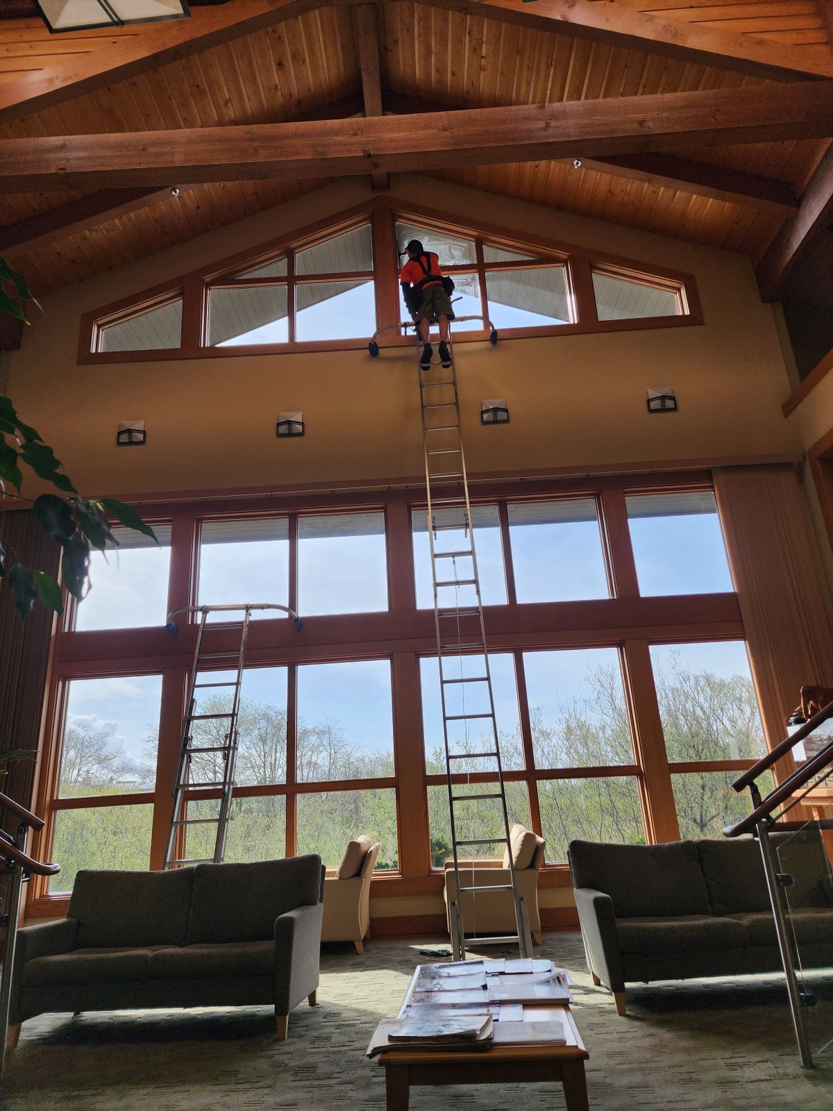 Crew member on a tall ladder cleaning vaulted great-room windows